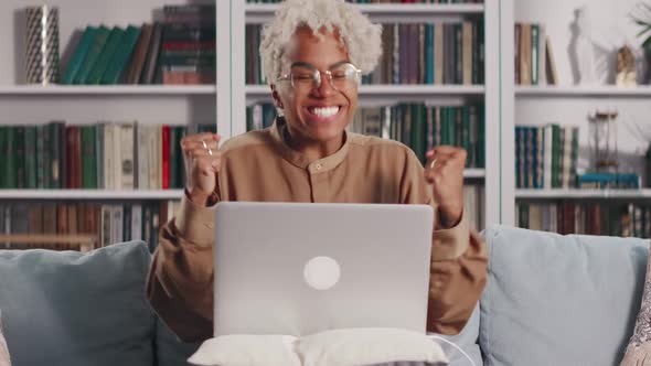 Young African American Woman with Laptop on Lap Overjoyed By News Sits on Sofa