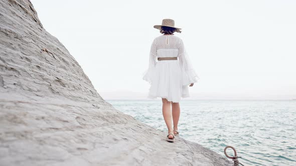 Stranger Woman in White Dress Walking on Clay Beach Near Mediterranean Sea