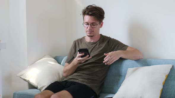 Young Modern Guy Communicates on the Phone While Sitting in the Room on the Couch