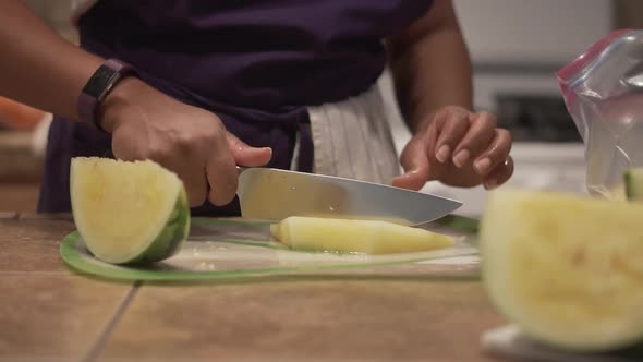 Closeup, black woman cutting yellow watermelon into slices in a home kitchen