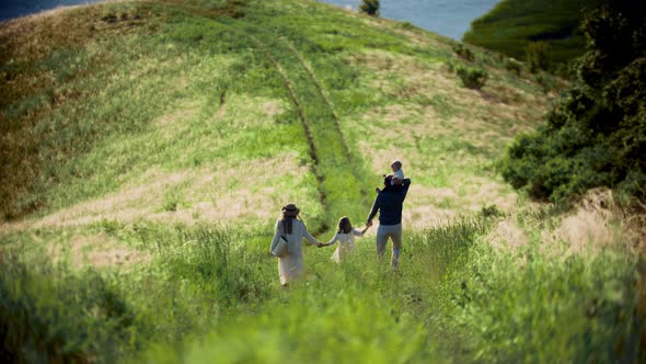 Young Family of Four Members Walking Down To the Green Field