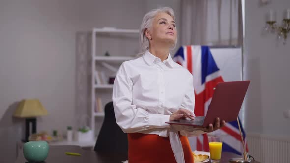 Thoughtful Beautiful Mature Businesswoman Standing with Laptop in Office Analyzing Business Strategy