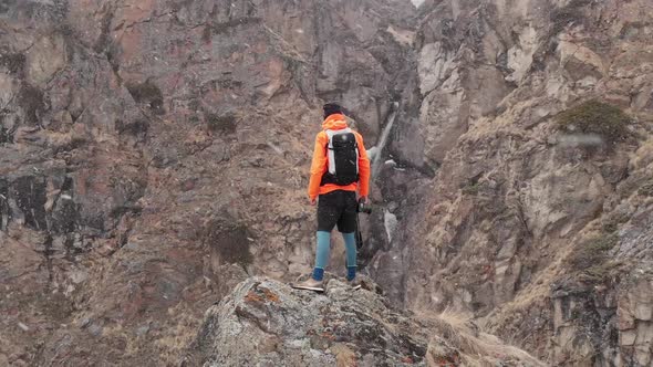 Aerial View of a Young Male Photographer with a Camera in His Hands Stands on a High Rock in a Gorge