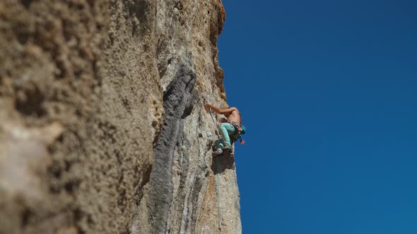 Bottom View of Muscular Strong Man Rock Climber Climbs on Vertical Cliff on Rock Wall on Blue Sky