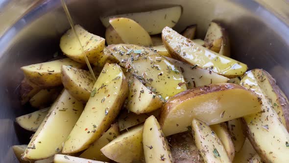 Cooking of homemade roasted potato wedges. Sprinkling the raw potato pieces with the olive oil