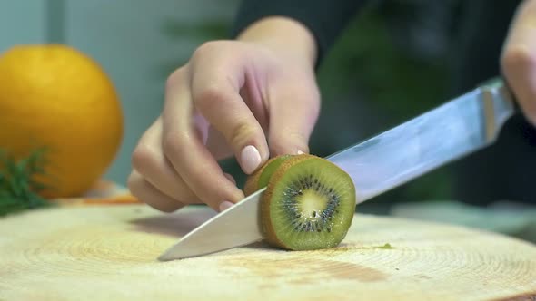 Slow motion womans Hand Slicing Kiwi. Knife Slicing Fresh Kiwi fruit Close Up on wooden cutting boar