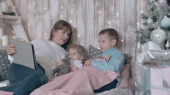 Blond Woman Looks at Little Girl and Boy Switches on Tablet