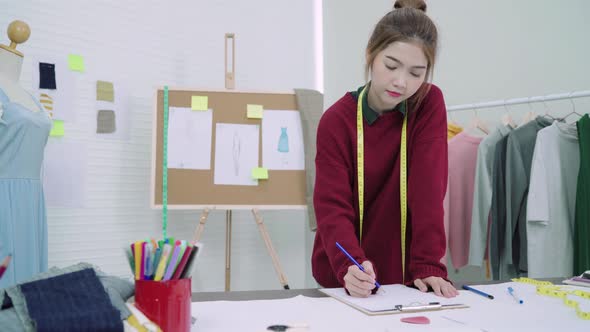 Young Asian woman fashion designer drawing using pencil and looking at paper in the workshop studio