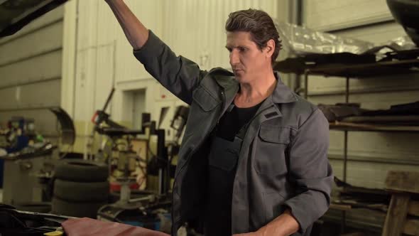 Video shot of the serious adult auto mechanic opening hood of the car while preparing to the repair