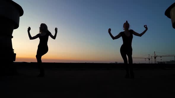 Two Women Dancing on Factory Roof in the Dark Against Sunset