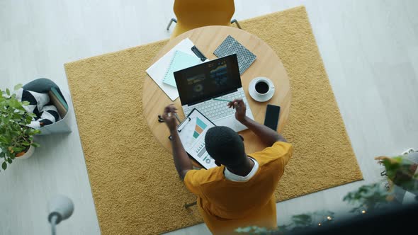 Top View of Businessperson Working with Laptop Studying Papers and Drinking Coffee in Kitchen