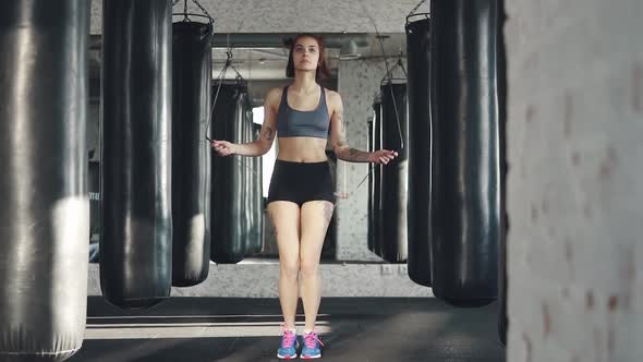 Girl Jumping Rope at the Gym on the Background of Punch Bags