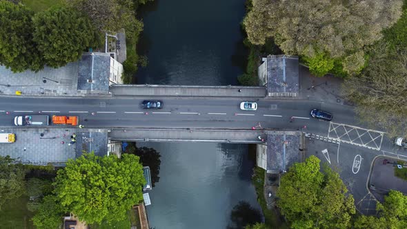 Aerial of directed traffic crossing a traditional old toll bridge across a quaint river