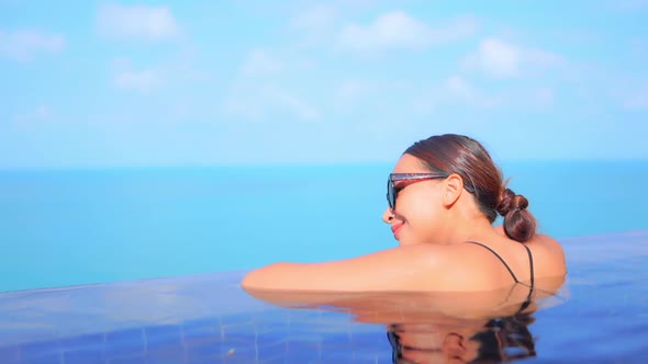 Woman leaning on edge of infinity swimming pool and looking to the sea