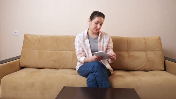 Young Woman Opens Envelopes with Bill and Dollars on Couch
