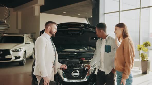 African Man and Caucasian Woman Talking with Competent Dealer While Choosing Car