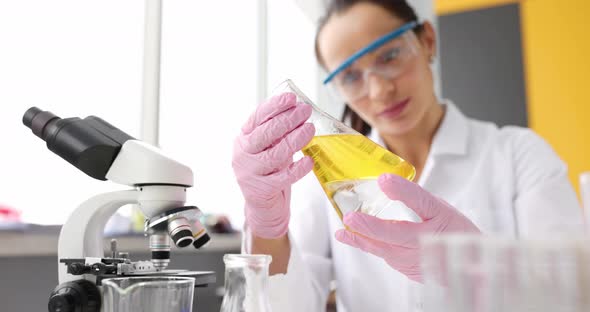 Chemist Scientist in Protective Rubber Gloves Holds Flask with Yellow Liquid Closeup