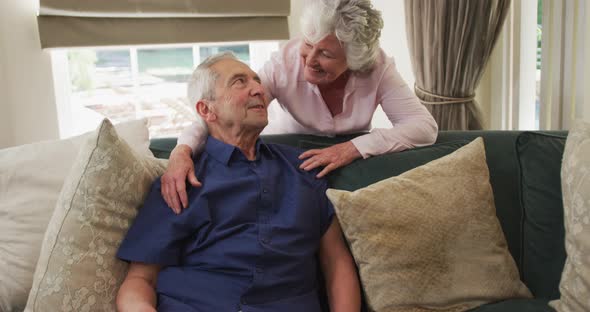 Senior caucasian couple embracing and smiling on sofa in living room in slow motion