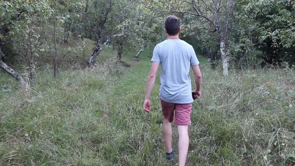 A man walks on a footpath in forest, daytime,  summer season. Young man filmed from behind while Wal