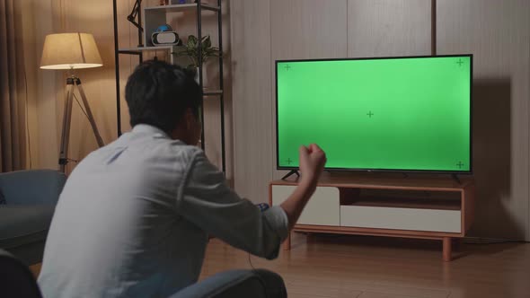Man Is Sitting On Coach And Playing At Video Game With Green Screen Tv And Celebrating Win