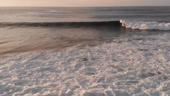 A drone flies over crashing waves as a surfer catches a wave at sunset on Maui, Hawaii's north shore