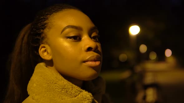 A Young Black Woman Looks Around in a City Park at Night  Face Closeup