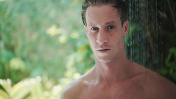 Young Man Takes Refreshing Shower Near Green Tropical Plants