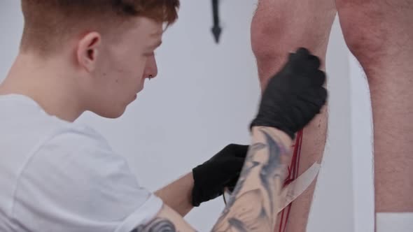 Young Man Tattoo Artist Taping a Duct Tape on the Leg on His Client