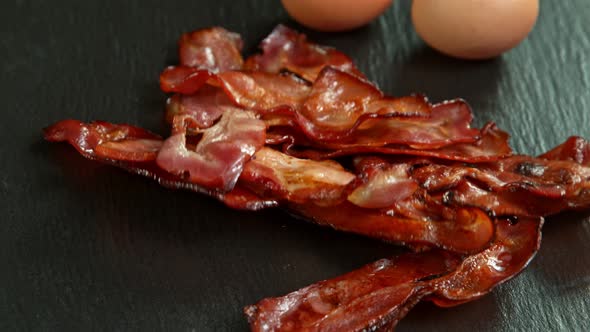 Super Slow Motion Shot of Roasted Bacon Slices Falling on Black Table at 1000 Fps