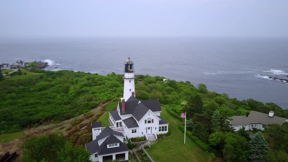 Aerial of lighthouse and villas on a green hill near the ocean