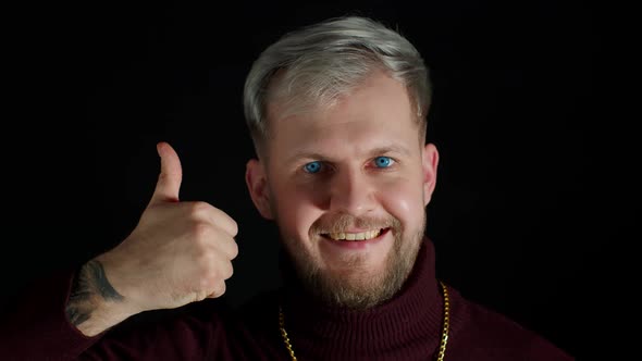 Smiling Man in Stylish Blouse Looking Approvingly at Camera Showing Thumbs Up on Black Background