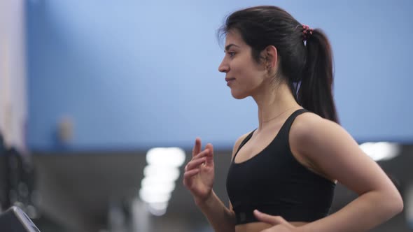 Motivated Slim Middle Eastern Sportswoman Running in Gym on Treadmill Indoors