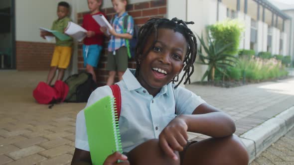 Video of happy african american boy holding books in front of school