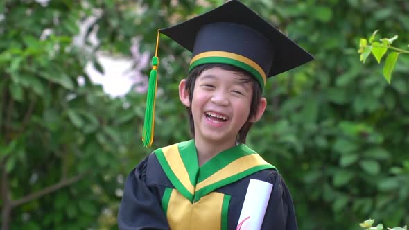 Happy Asian Child In Graduation Gowns Holding A Certificate