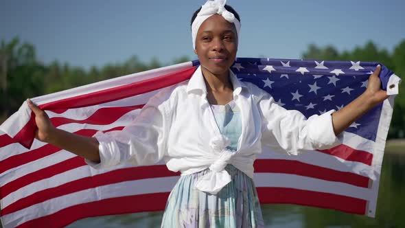 Proud African American Young Woman Wrapping in USA Flag in Slow Motion Looking at Camera Smiling