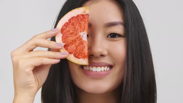 Asian Lady Holding Grapefruit HalfSlice Near Face Posing White Background