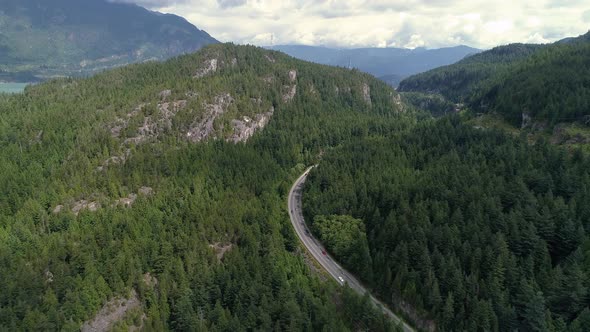 Helicopter View Of Cars Traveling Scenic Highway Into Thick Green Forest Mountains
