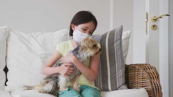 Girl wearing face mask holding her pet dog at home