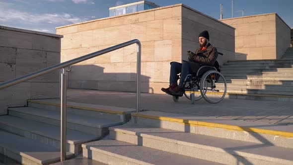 Disabled Man in Wheelchair is Standing in Front Stair in City Using Map in App in Smartphone