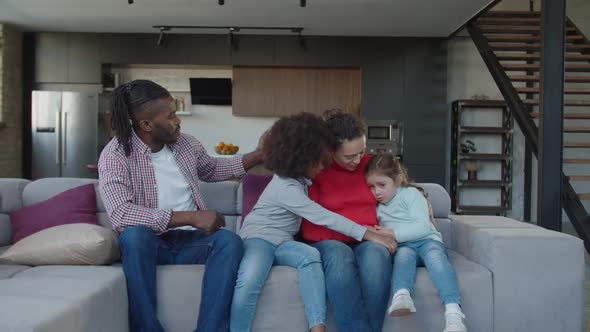 Positive Mother and Older Multiethnic Sister Comforting Upset Little Girl in Domestic Room