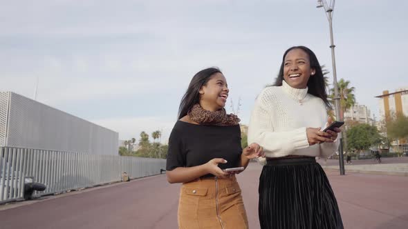 Two womans walking in a city while using a mobile phone and laughing