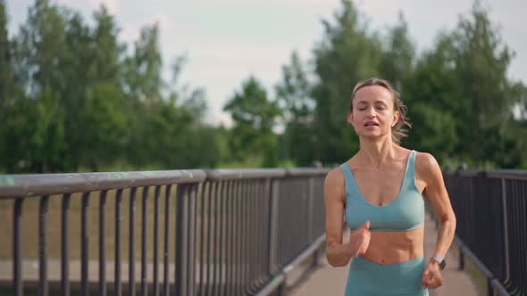 A Fit Young Caucasian Woman Running Intensively in Slow Motion on the Bridge in the Morning