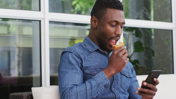 African american businessman using smartphone and eating croissant in cafe