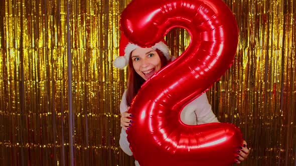 Woman in Santa Hat with Red Figure Two on Background of Shimmering Golden Tinsel