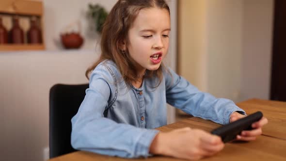 Happy kid girl playing game on mobile phone at home