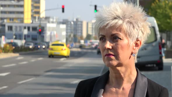 A Middle-aged Woman Stands By a Road in an Urban Area and Looks Around - Closeup