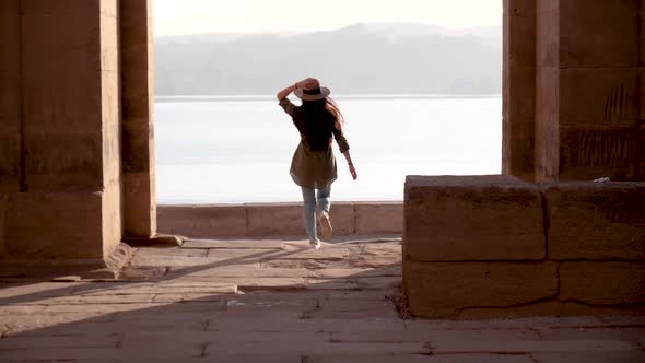 Caucasian woman with hat running through the ruins of Temple of Philae with lake in background in As