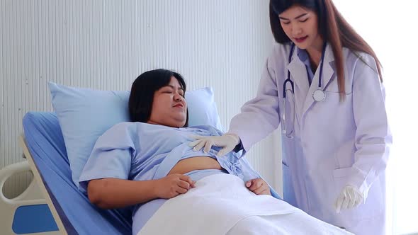 Asian female doctor talking to obese female patient lying in hospital bed