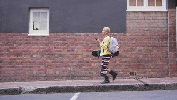 Mixed race woman walking on street holding her skateboard and her phone