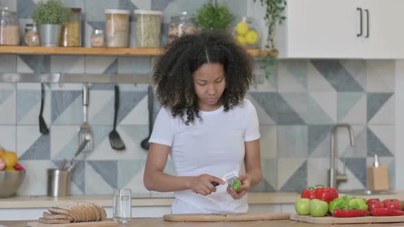 Attractive Young African Woman Peeling Cucumber in Kitchen